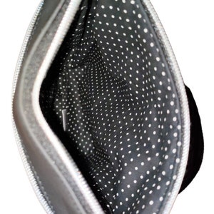 May include: Black crossbody bag with a silver zipper and a black and white polka dot lining.