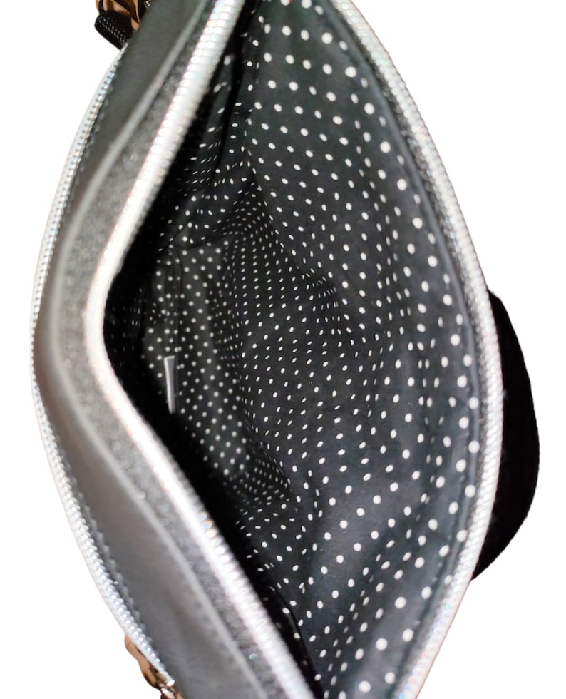 May include: Black crossbody bag with a silver zipper and a black and white polka dot lining.