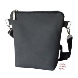 May include: A black crossbody bag with a zipper closure and a silver zipper pull. The bag has a black adjustable strap with a silver clasp.
