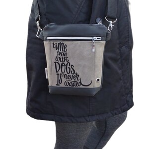 May include: A gray and black crossbody bag with a zipper closure. The bag has a quote embroidered on it that reads "Time spent with dogs is never wasted."