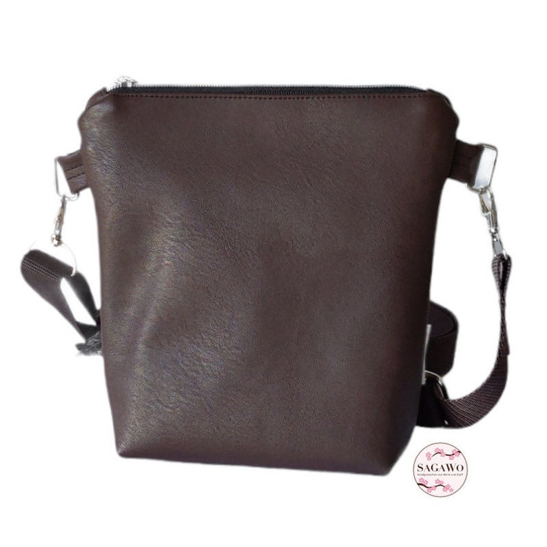 May include: A brown leather crossbody bag with a zipper closure and an adjustable strap. The bag has a silver hardware accent.