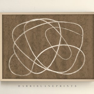 May include: Abstract art print with a brown textured backdrop and a white, continuous line drawing. The artwork is framed in a light beige wooden frame. The text "HARRIS LANE PRINTS" is printed at the bottom.