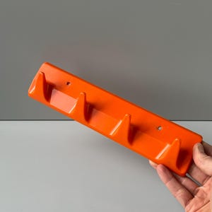 May include: Orange plastic wall mounted coat rack with four hooks.