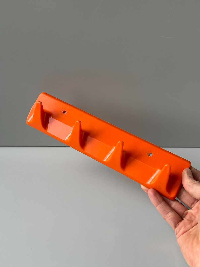May include: Orange plastic wall mounted coat rack with four hooks.