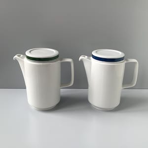 Könnte beinhalten: Zwei weiße Kaffeekannen aus Keramik mit Deckeln. Eine Kanne hat einen grünen Streifen um den Deckel und die andere einen blauen Streifen.