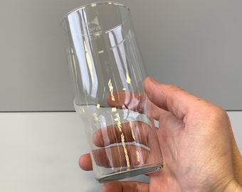 May include: A clear glass drinking glass with a slightly curved shape. The glass is empty and appears to be made of thick glass.