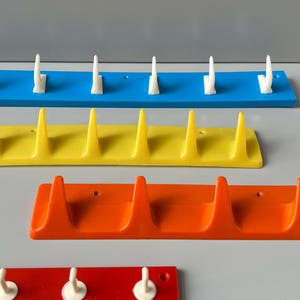 May include: Four sets of wall-mounted hooks in blue, yellow, orange, and red. Each set has a different number of hooks, ranging from three to five.