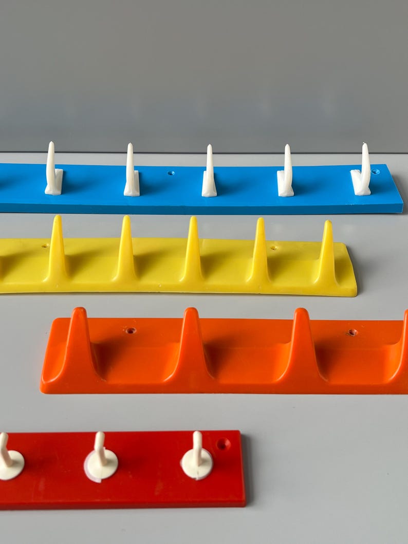May include: Four sets of wall-mounted hooks in blue, yellow, orange, and red. Each set has a different number of hooks, ranging from three to five.