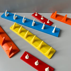 May include: Five different coloured wall mounted hooks with white plastic hooks. The hooks are in red, yellow, blue, and orange.