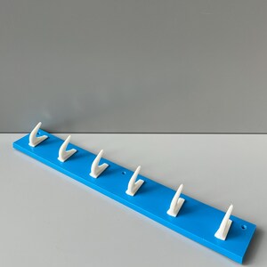 May include: A blue wooden wall-mounted coat rack with six white plastic hooks.