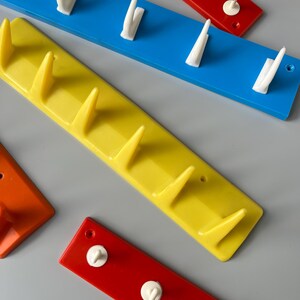 May include: Four wall-mounted hooks in different colours: red, yellow, blue and orange. Each hook has a different number of white plastic hooks.