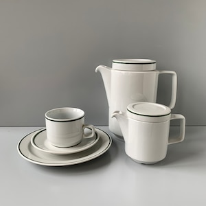 Peut inclure: Une cafetière en céramique blanche avec une bordure et un couvercle verts, un pot à crème assorti et une tasse et une soucoupe avec une bordure verte.