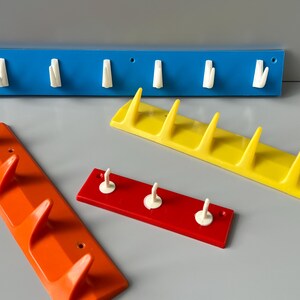 May include: Four different coloured plastic wall mounted coat racks with white hooks. The racks are blue, yellow, red and orange.