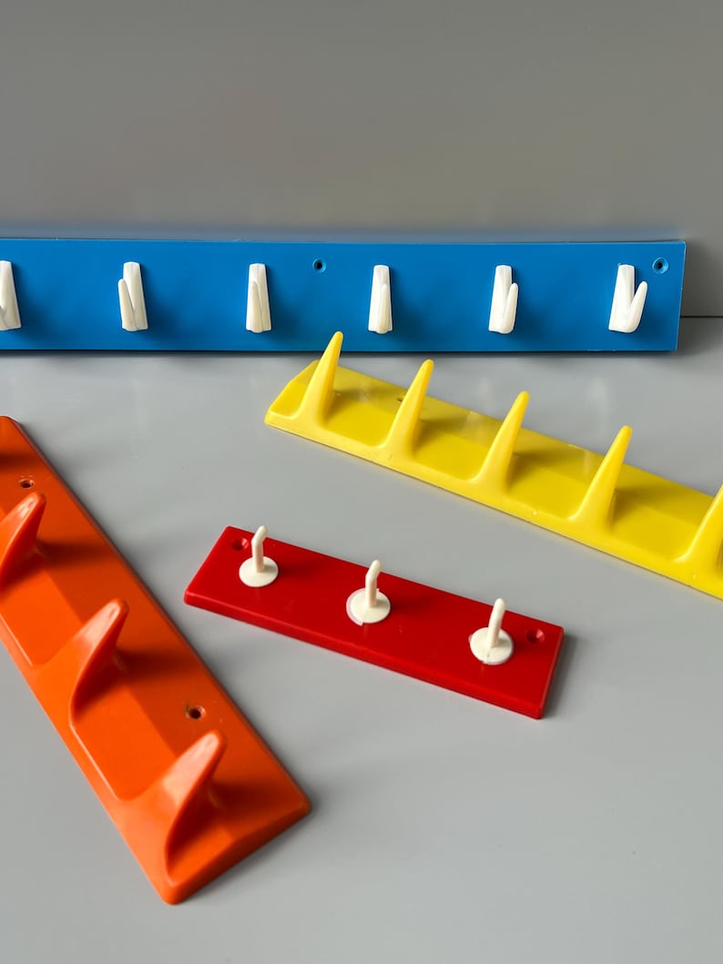 May include: Four different coloured plastic wall mounted coat racks with white hooks. The racks are blue, yellow, red and orange.