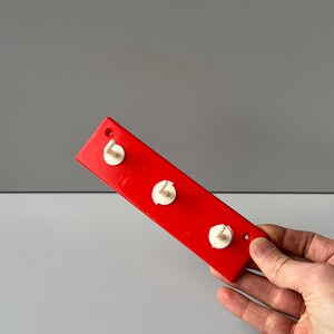 May include: A red plastic wall-mounted hook rack with three white plastic hooks.