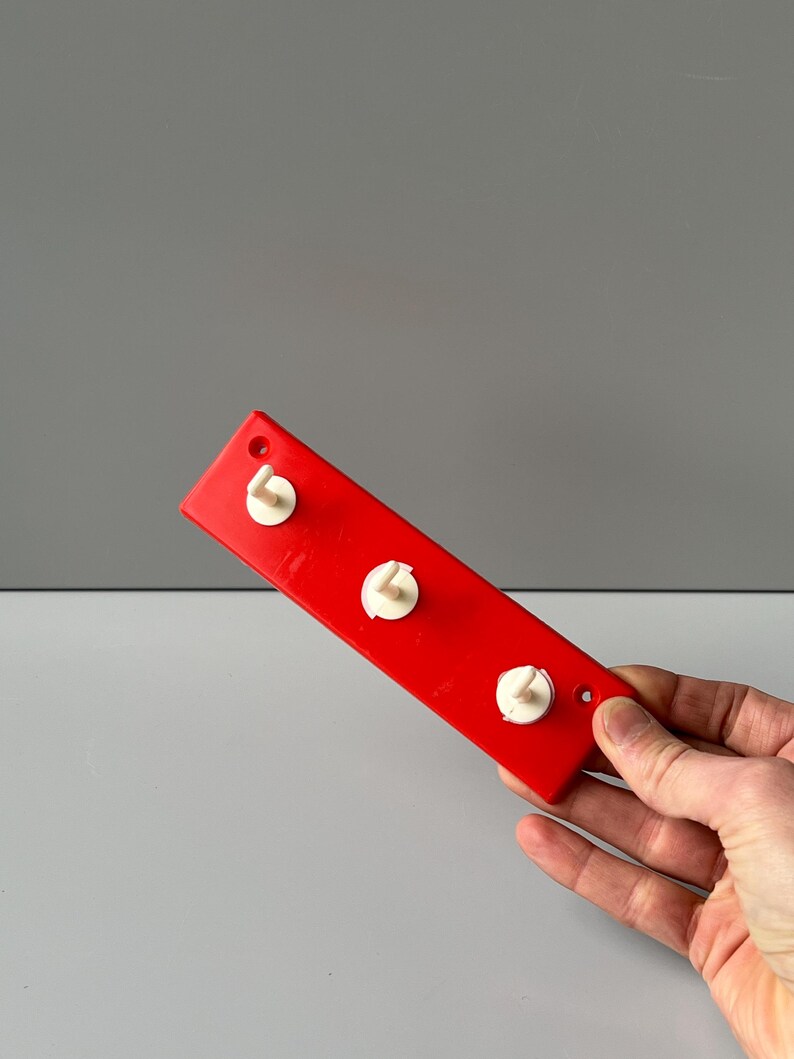 May include: A red plastic wall-mounted hook rack with three white plastic hooks.