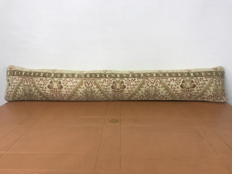 May include: A long, rectangular pillow with a beige background and a repeating pattern in shades of brown and red. The pillow is placed on a brown surface.