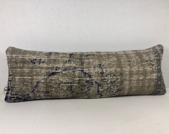 May include: A long, rectangular throw pillow with a brown and blue patterned design. The pillow is made of a soft, woven fabric and has a subtle distressed look.