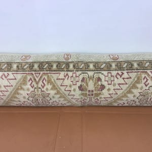 May include: Rolled-up beige and brown patterned rug. The rug features a repeating geometric design with floral elements in shades of beige, brown, and burgundy. The rug is rolled up, showing the detailed pattern.