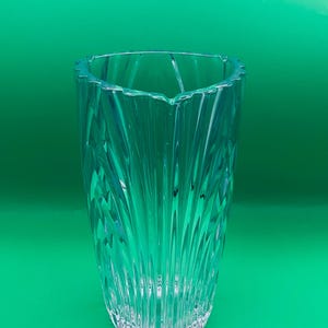 May include: A clear, blue-tinted glass vase with a textured, vertical pattern. The vase has a wide, triangular opening and a slightly flared base. The background is a solid, bright green.