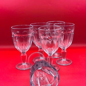 May include: Six clear glass wine glasses with a textured design on a red background.