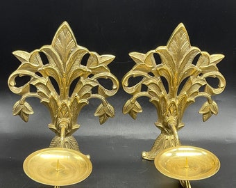 May include: A pair of ornate gold-toned metal candle holders with a floral design. Each holder has a circular candle cup.