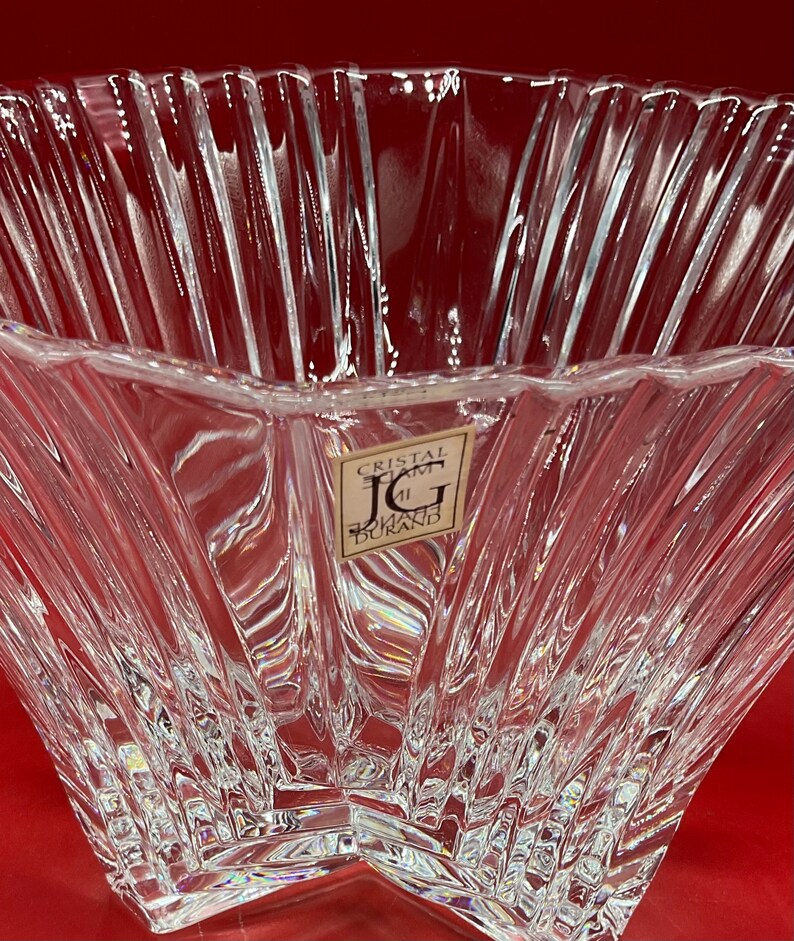 May include: A clear glass bowl with a star-shaped base and a textured, ribbed design. The bowl has a label that reads "Cristal d'Arques J.G. Durand".