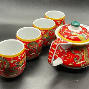 May include: A red and gold Chinese tea set with a dragon design. The set includes a teapot and four cups.