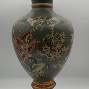 May include: A tall, decorative vase with a dark green base and a flared top. The vase features a floral design in shades of red, gold, and cream. The base and rim have gold accents. This elegant vase is suitable for home decor.