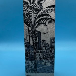 May include: A white ceramic vase with a black and white design of a palm tree and buildings. The vase has a crackled glaze.