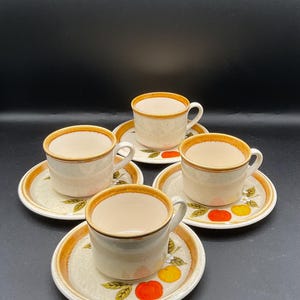 May include: Set of four white ceramic teacups and saucers with a brown rim and orange and yellow fruit design.