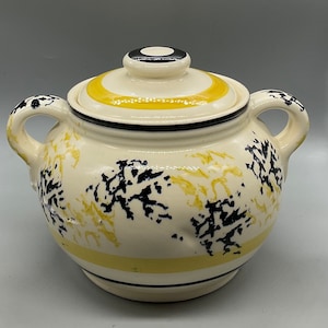 May include: A white ceramic sugar bowl with a yellow and black striped lid. The bowl has a black and yellow floral design.