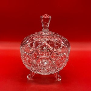 May include: A clear glass candy dish with a lid and three legs. The dish has a diamond pattern.