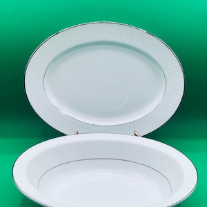 May include: A white oval serving platter and a white round bowl with a silver rim and a delicate floral pattern.