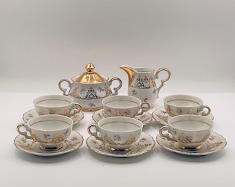 May include: A white porcelain tea set with gold trim and floral designs. The set includes a teapot, creamer, sugar bowl, and six cups and saucers.