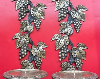 May include: A pair of ornate brass wall candle holders with a grapevine design. Each holder features a circular tray with a decorative border and a single candle holder.