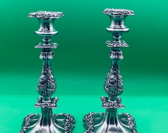 May include: A pair of silver candle holders with ornate designs. The candle holders have a square base with a decorative floral pattern and a tall, slender stem with a round candle cup.