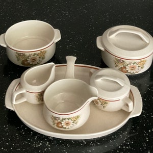 May include: A set of five white ceramic dishes with floral patterns. The dishes include a small bowl, a creamer, a gravy boat, a sugar bowl with a lid, and a serving platter.