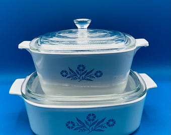 May include: A set of two white casserole dishes with blue floral designs. The dishes are made of glass and have lids.