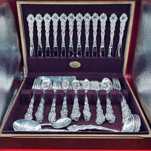 May include: A wooden box with a velvet lining containing a set of silver flatware. The flatware is arranged in two rows, with the handles facing up. The box has a label that reads "James River."