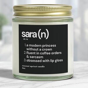 Puede incluir: Una vela de vidrio en un frasco con tapa dorada y una etiqueta negra que dice "sara (n)" SE.ra 1. a modern princess without a crown 2. fluent in coffee orders & sarcasm 3. obsessed with lip gloss coconut apricot candle 4oz
