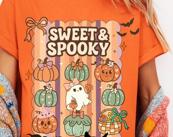 May include: Orange t-shirt with a "Sweet & Spooky" graphic. The design features cartoon pumpkins, a ghost, a black cat, spiders, and bats. The shirt has short sleeves and a crew neck.