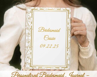 May include: A white journal with a gold floral border and the text "Bridesmaid Cassie 09.22.25". The journal is labeled "Personalized Bridesmaid Journal - Any Role • Any Name • Any Date". The journal is held by a person.