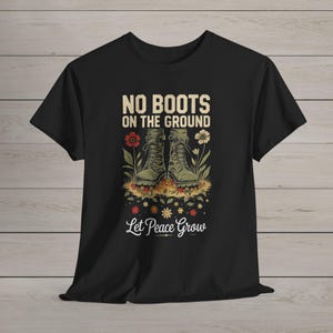 May include: Black t-shirt with the text "NO BOOTS ON THE GROUND" above an illustration of combat boots surrounded by flowers. The phrase "Let Peace Grow" is below the boots. The design is in shades of green, red, and beige.