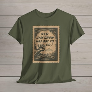 Puede incluir: Camiseta verde oliva con un gráfico vintage. El gráfico, que se asemeja a un sello postal, muestra el texto "OLD JIM CROW HAS GOT TO GO!" con un puño cerrado y texto sobre derechos civiles. La camiseta está hecha de un material suave.