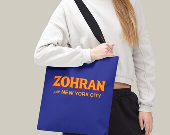 Op de afbeelding: Een blauwe draagtas met de naam "ZOHRAN" in oranje en gele letters. De tekst "for NEW YORK CITY" staat eronder in het oranje. De tas heeft een zwarte schouderriem.