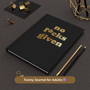 Puede incluir: Un diario negro con el texto dorado "no f*cks given". Clips dorados, lápices y una decoración geométrica dorada rodean el diario. La parte inferior de la imagen tiene el texto "Funny Journal for Adults."