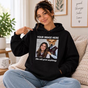 May include: A black hooded sweatshirt featuring a central graphic print. The print displays a person and a dog wearing matching argyle sweater vests, with the text YOUR IMAGE HERE above and (We will print anything) below the image.