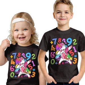 May include: Two children wearing black t-shirts featuring a unicorn design. The unicorn is dabbing, surrounded by numbers and math symbols. The shirts have a rainbow mane and tail, with the text "+7892, 460=3, 51".