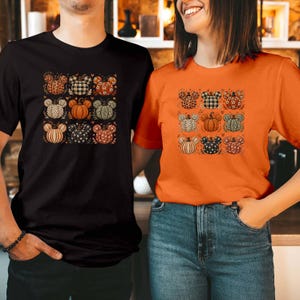 Könnte beinhalten: Ein schwarzes T-Shirt und ein orangefarbenes T-Shirt, die jeweils ein Raster aus neun kürbisförmigen Grafiken in Form von Mausohren zeigen. Die Kürbisse weisen verschiedene Muster wie Leopardenmuster, Karos, Blumen und Punkte auf.